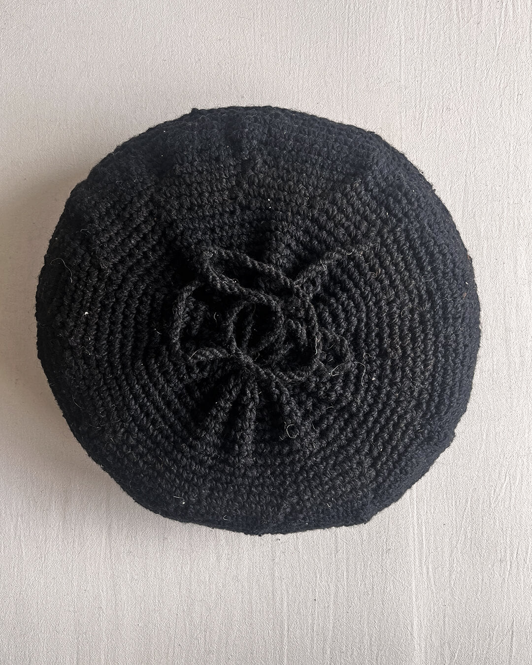 Back of a Black round cushion made of handwoven wool, with visible woolen tie closure.