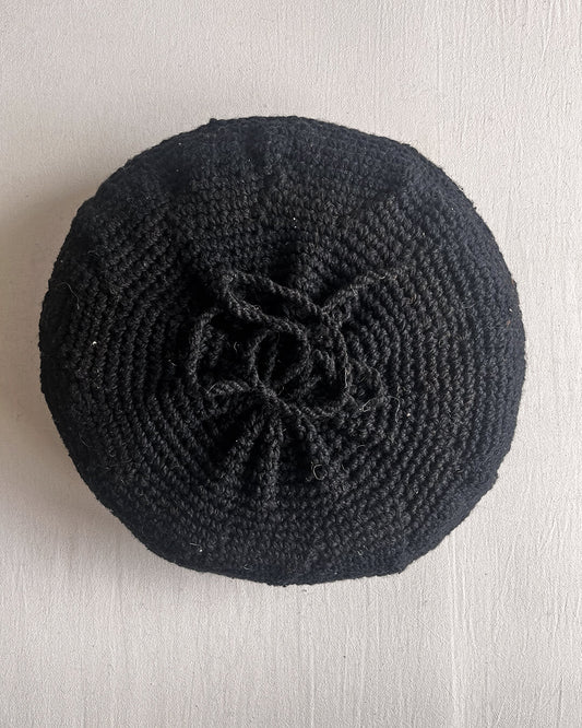 Back of a Black round cushion made of handwoven wool, with visible woolen tie closure.