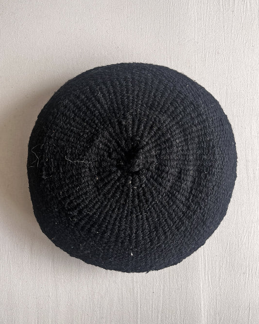 Black-colored round cushion made of handwoven wool, shown from the front.