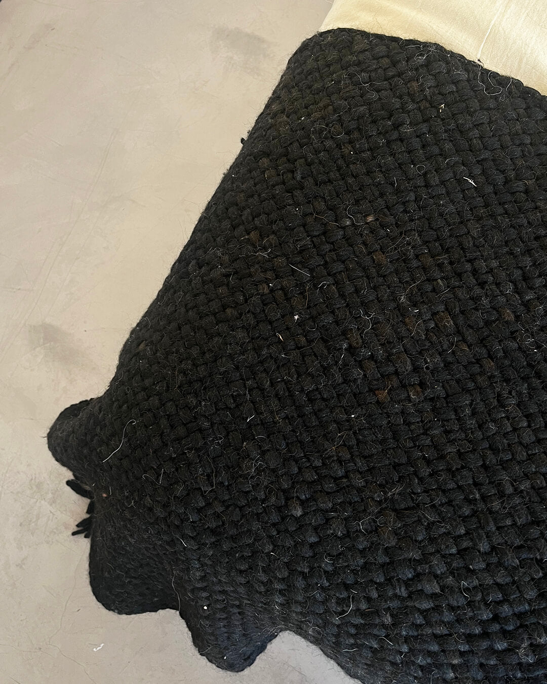 Black wool throw over the edge of a light-colored bed, showing the full woven structure.