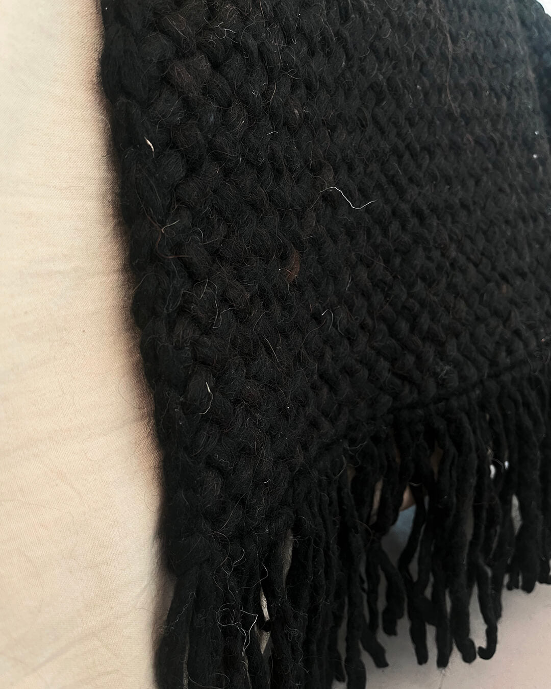 Detail of Black wool throw draped over a light couch, focusing on the weave and fringe.