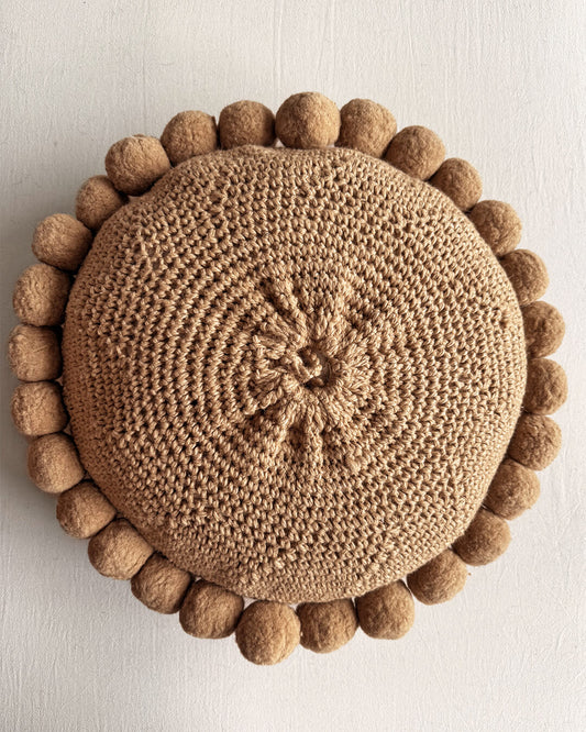 Back of a camel-colored round wool cushion with visible woolen cords.