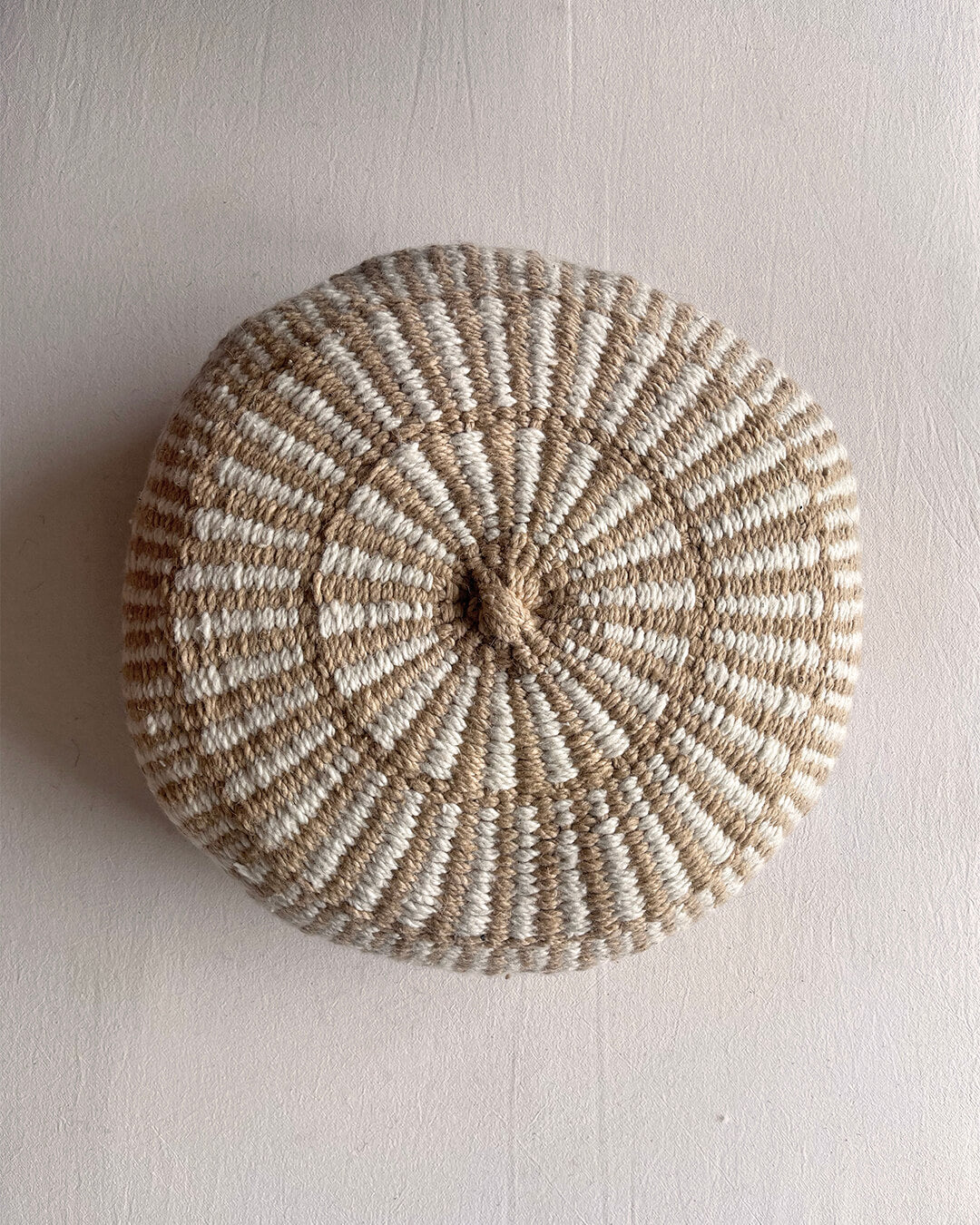 Round cushion in Beige-Sand and Natural White with comb-pattern design, shown from the front.