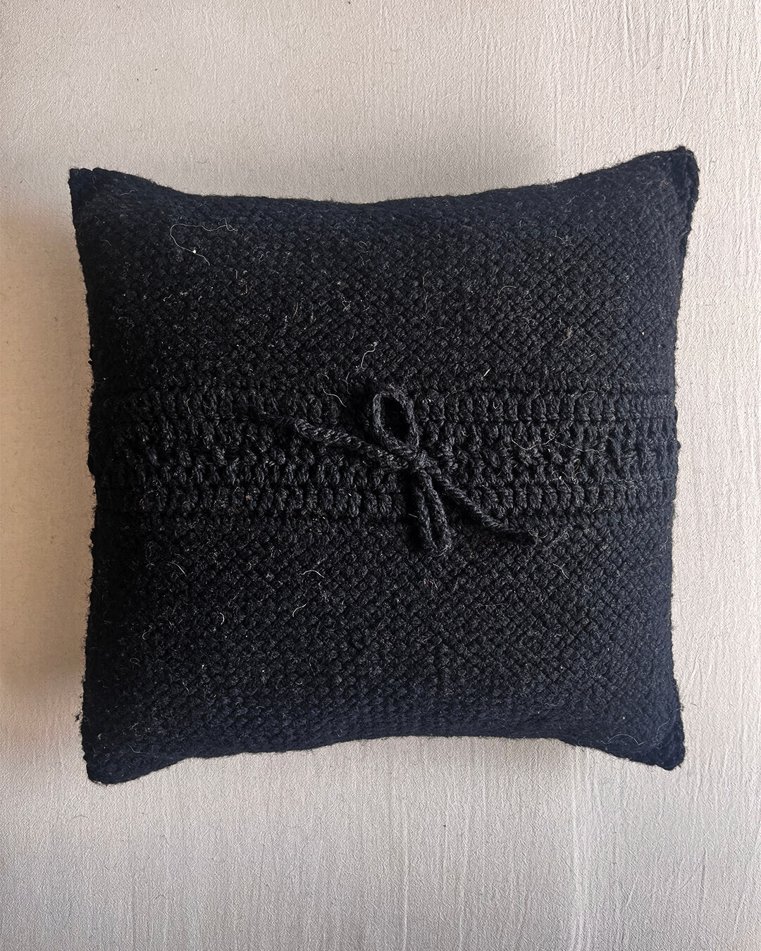 Black square wool cushion, shown from the back with woolen tie closure.