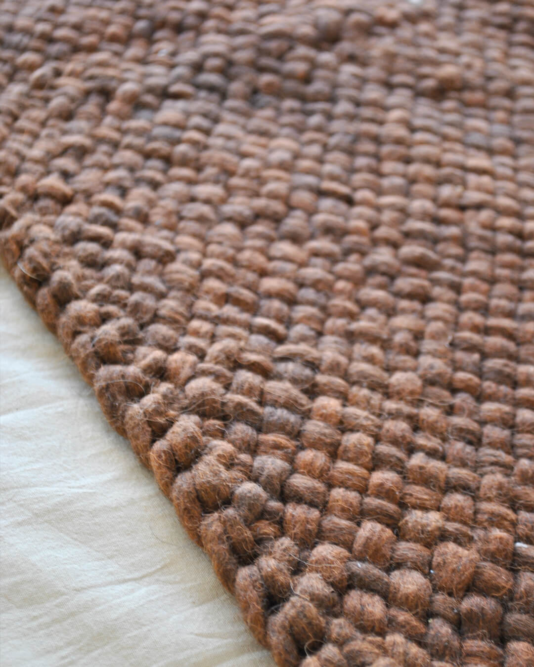 Close-up of the Chocolate Brown wool throw’s weave lying flat on a bed.