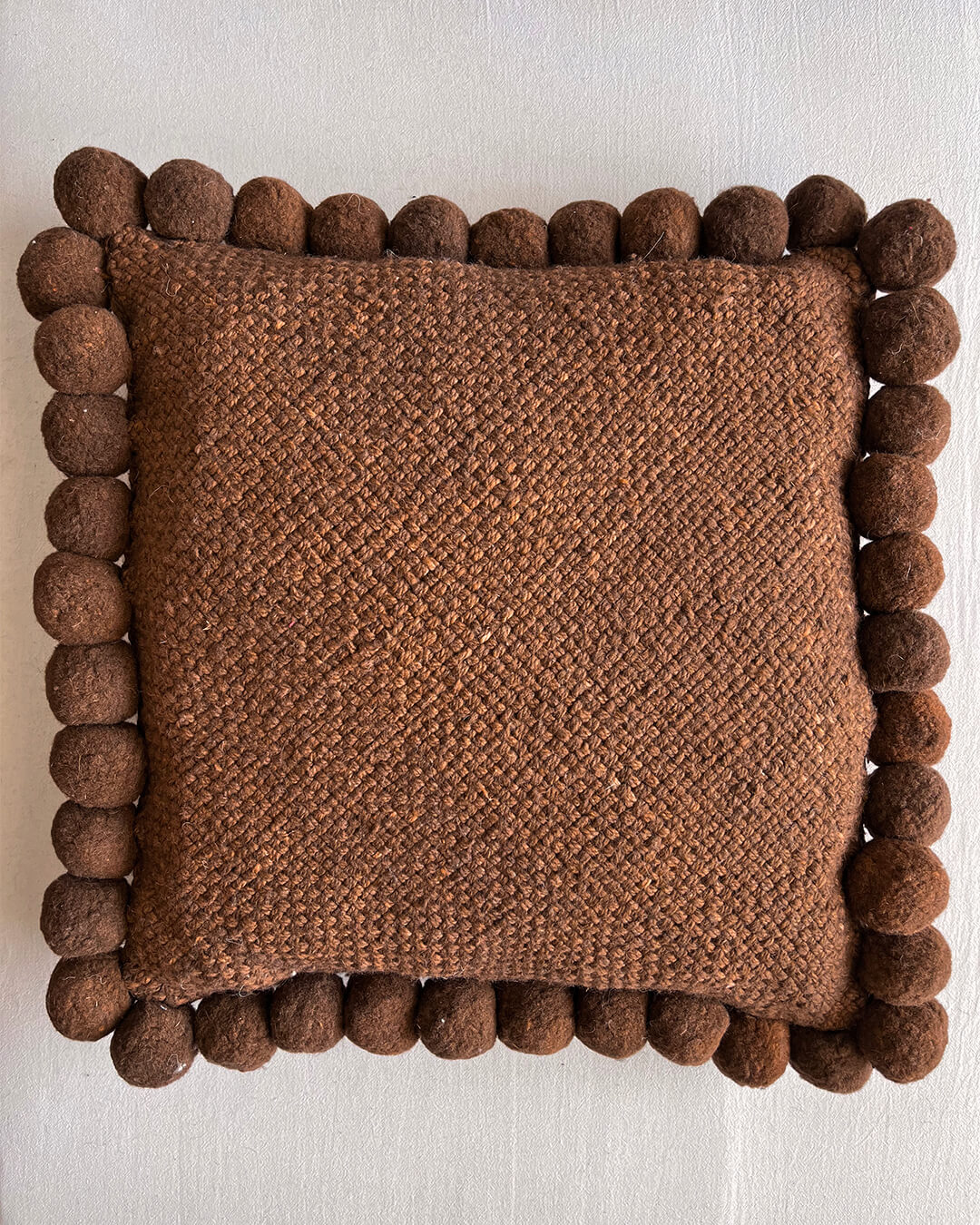 Chocolate Brown square cushion with handmade pom poms, shown from the front.
