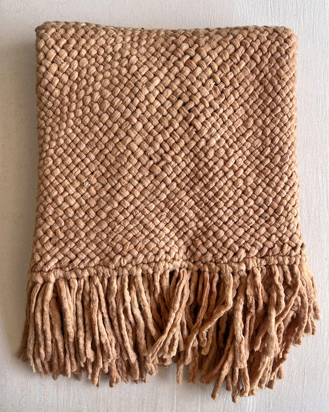 Folded wool throw in Camel color with fringes, placed on a flat surface.