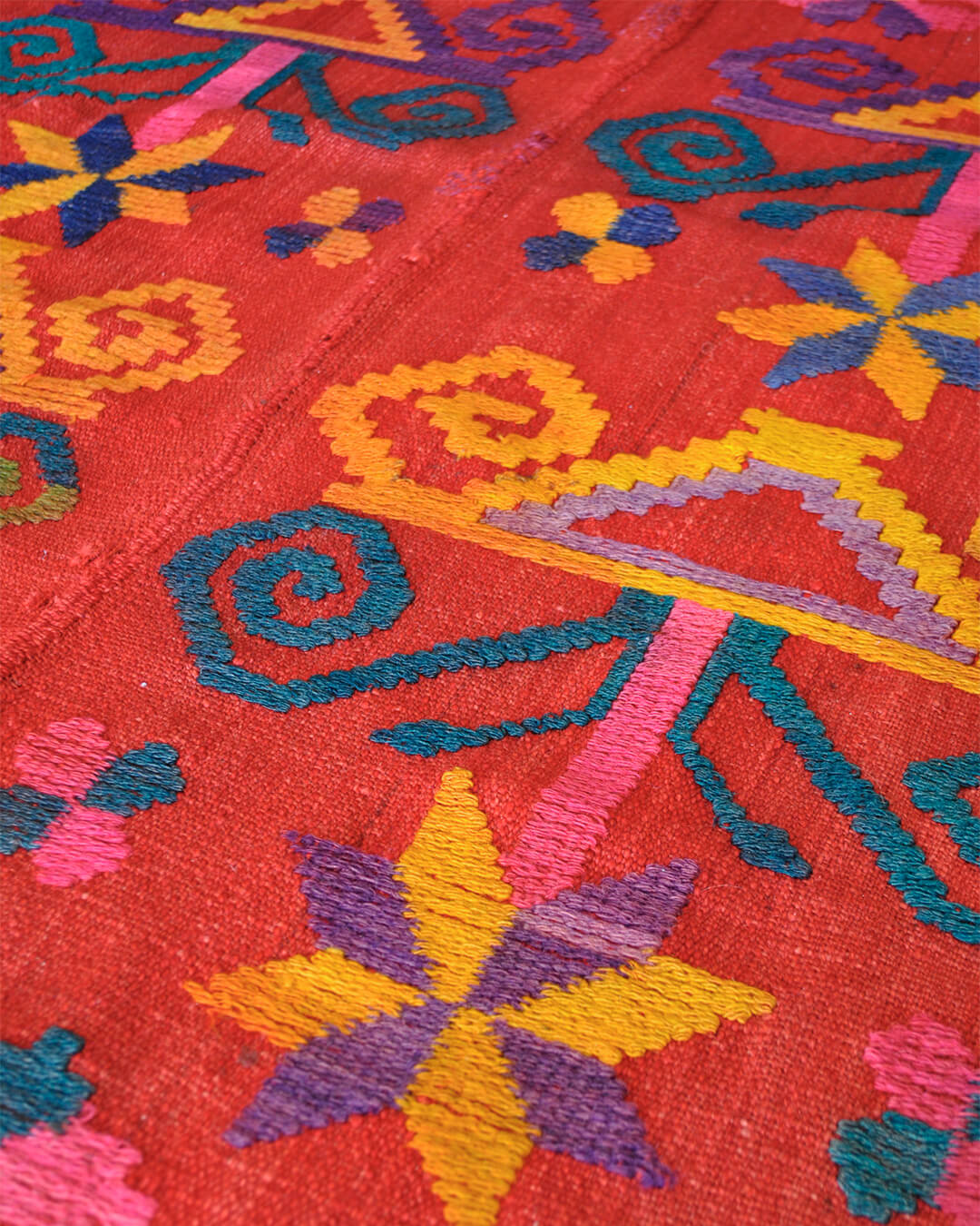 Close-up of CHACO frazada showing detailed handwoven geometric patterns in vivid red, yellow, pink, and blue tones.