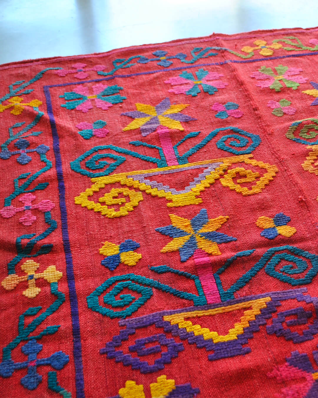 Handwoven CHACO frazada with intricate multicolor patterns on a red background, featuring traditional shapes and vibrant contrasts.