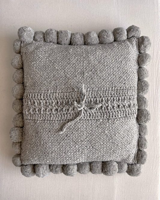 Gray-colored square cushion with handmade pom poms, shown from the back.