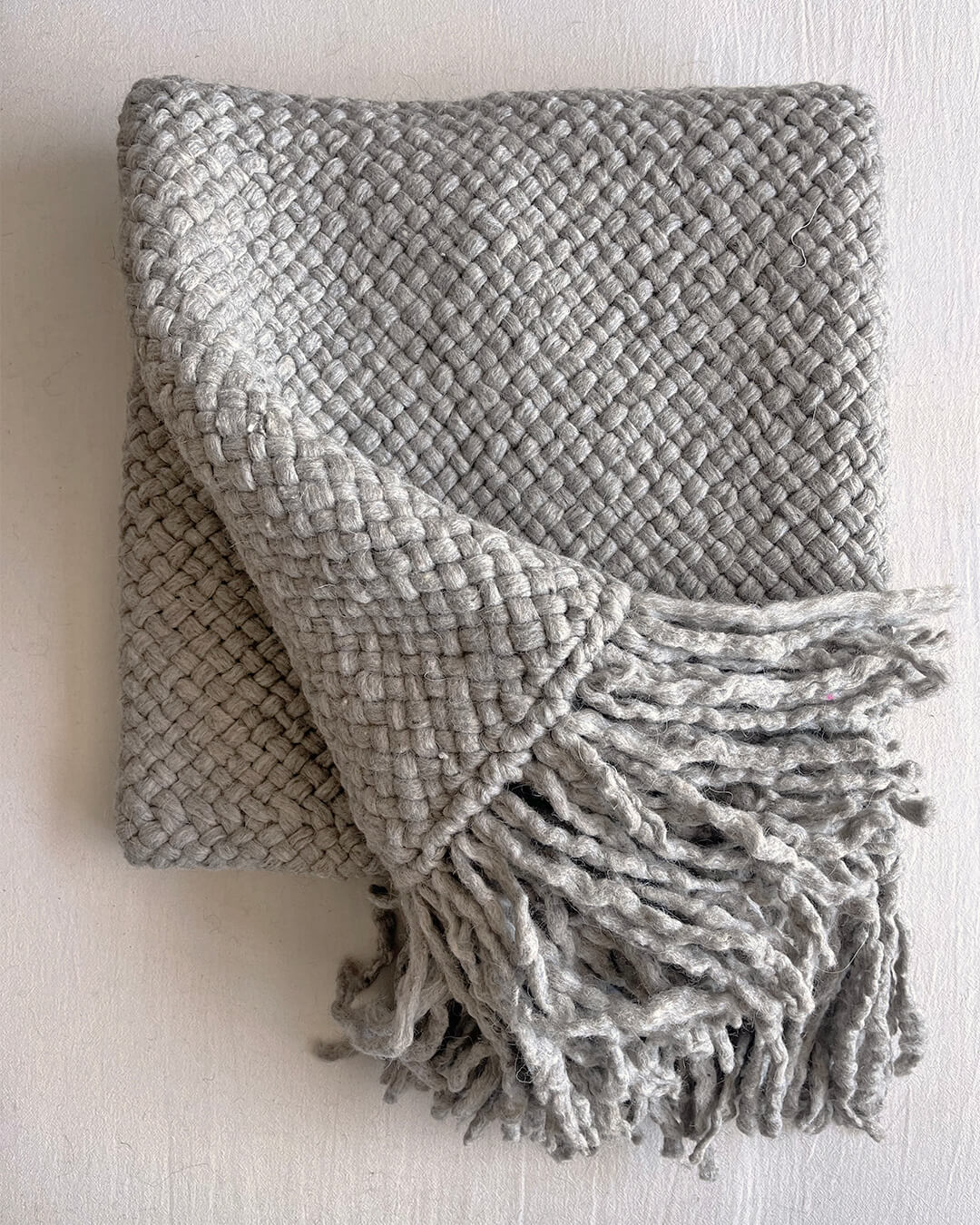 Soft Gray wool throw folded with fringes displayed across the front.