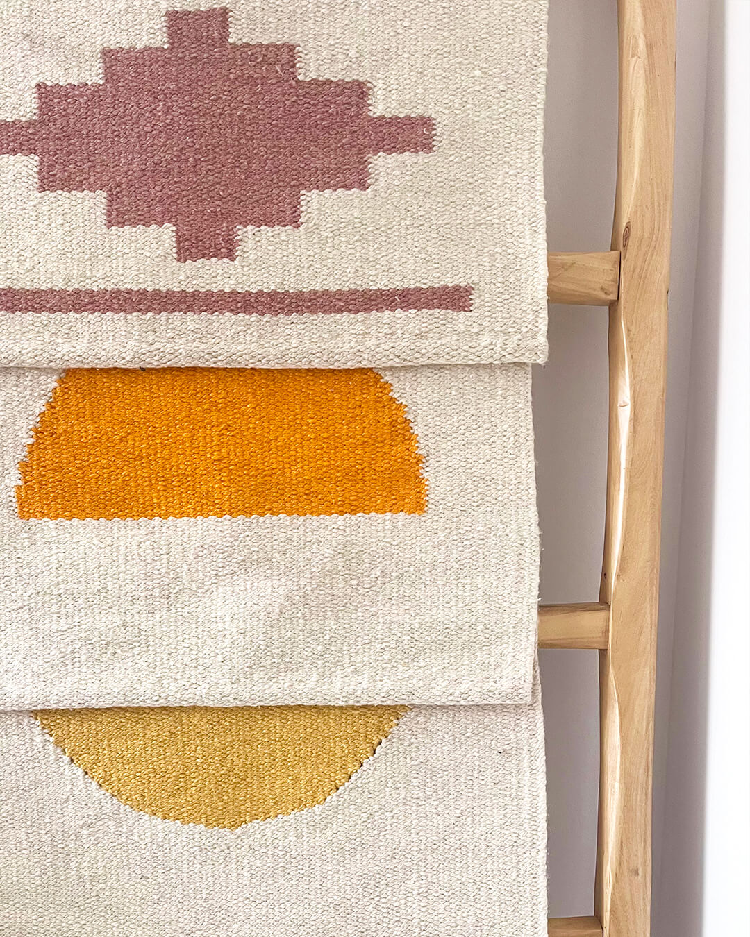 Handwoven CHACO Mini Rugs displayed on a wooden ladder, featuring geometric and sun-inspired designs in earthy tones.