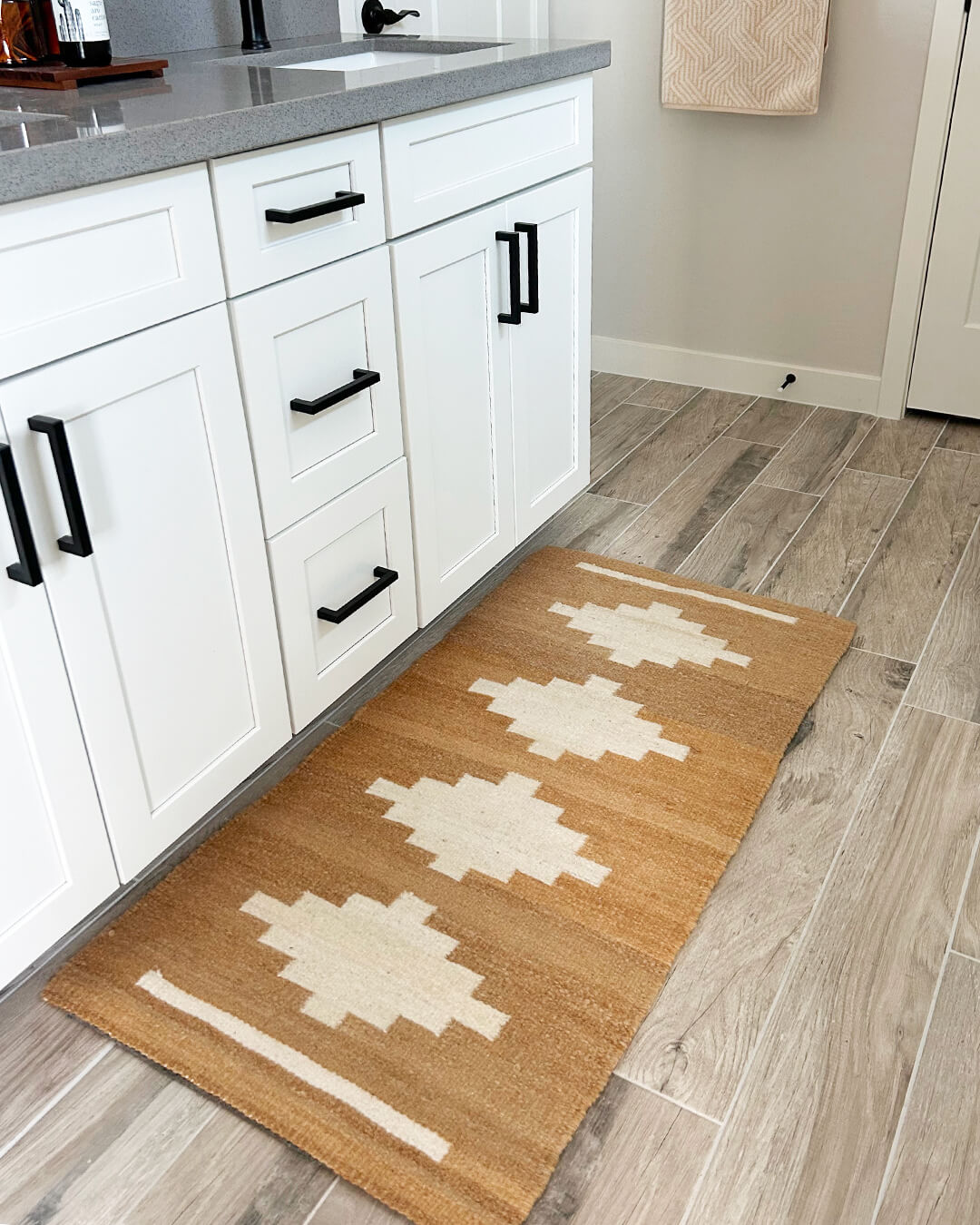 Handwoven CHACO Mini Rug placed in a bright kitchen, featuring a natural brown base with white geometric design.