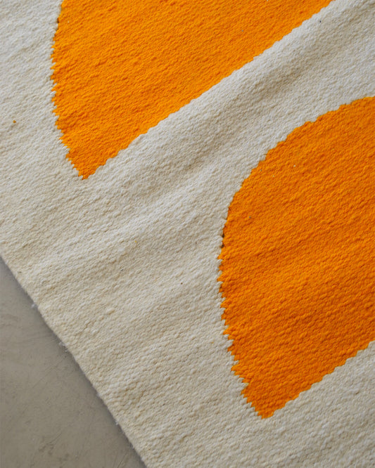 Close-up of the CHACO Mini Rug showing two bright orange semicircles woven on a natural white wool base.