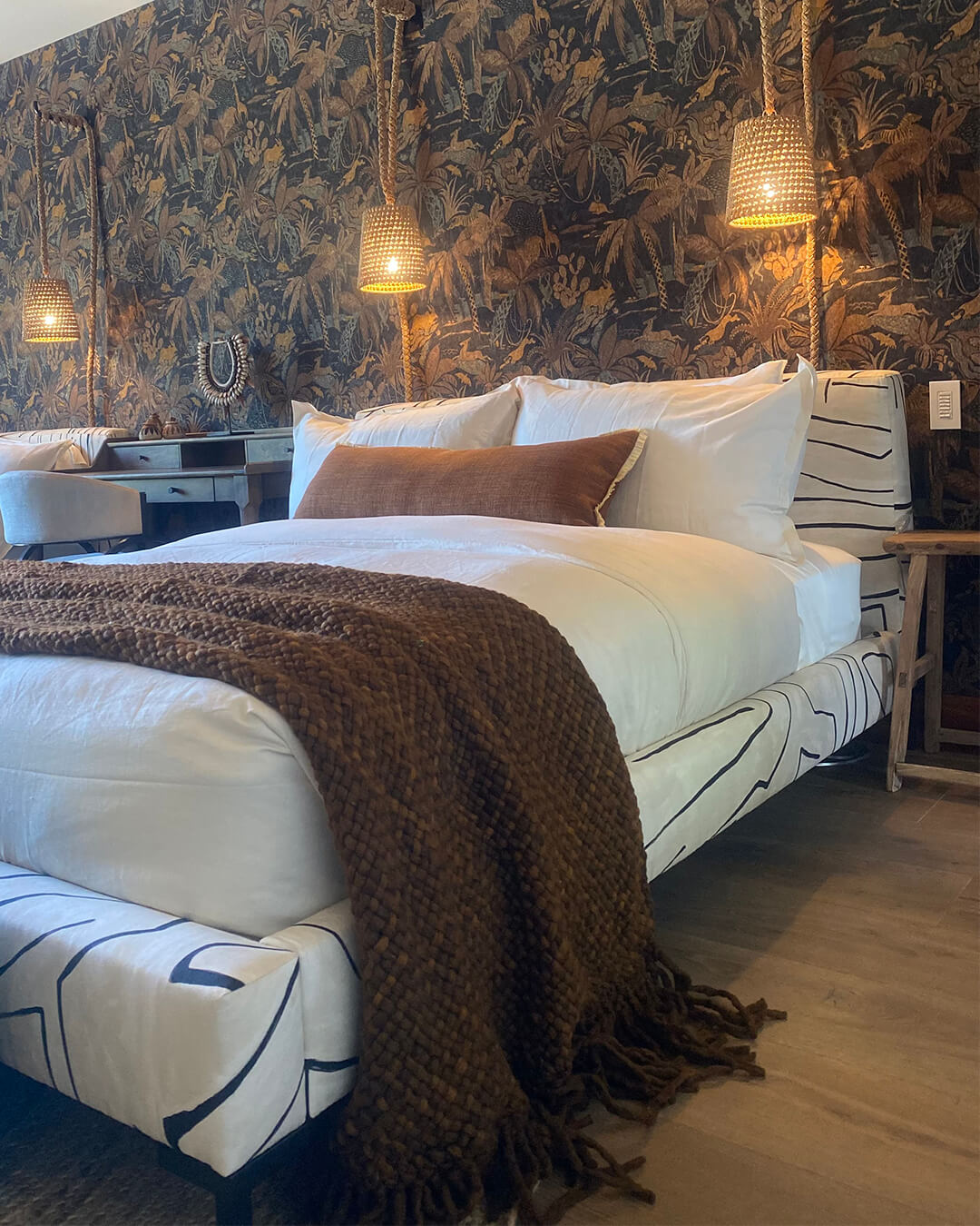 Chocolate Brown wool throw draped at the foot of a bed in a bedroom with patterned wallpaper.