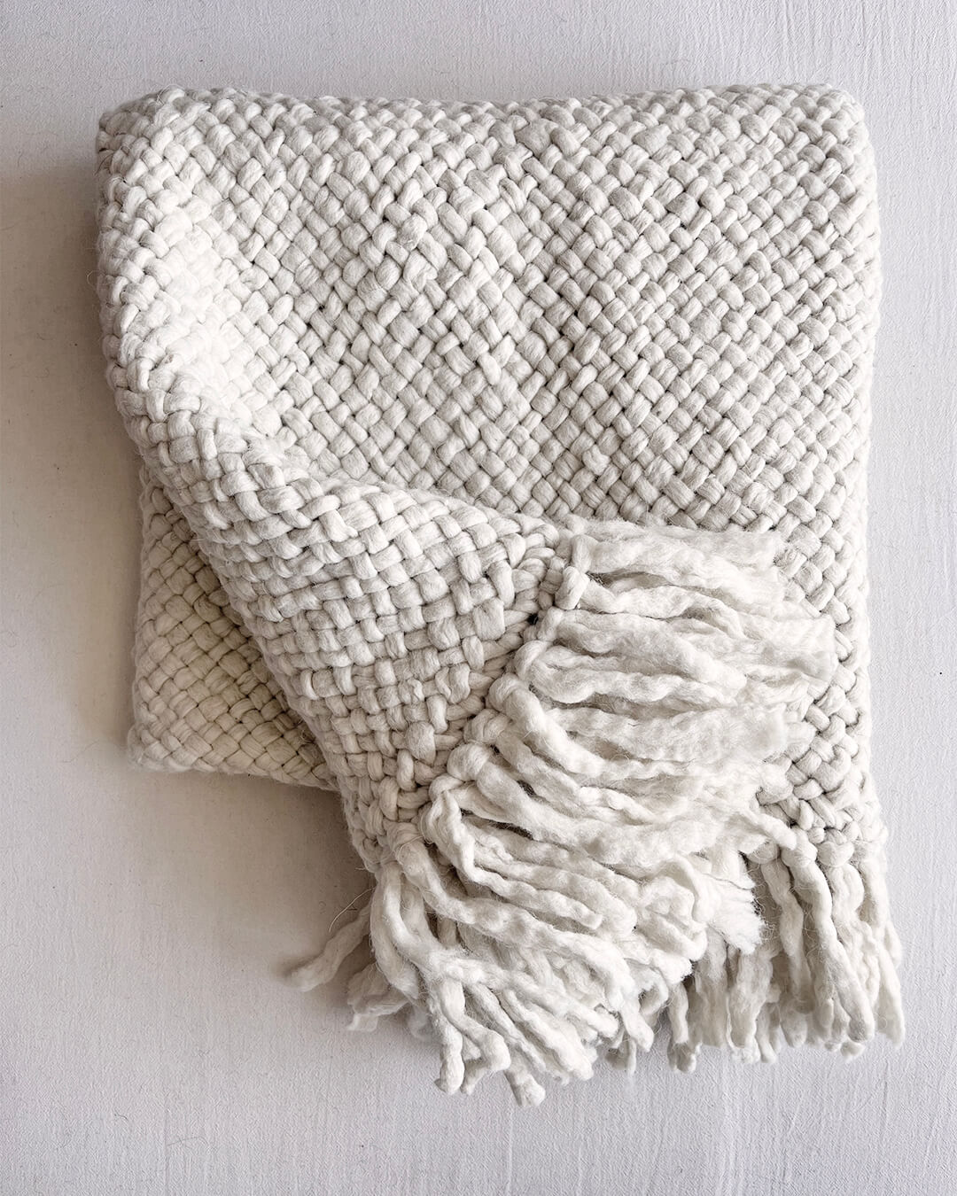 Natural White wool throw with front-facing fringe detail, folded neatly.
