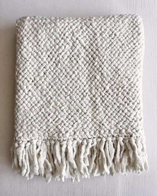 Folded Natural White wool throw with visible fringe on a neutral background.
