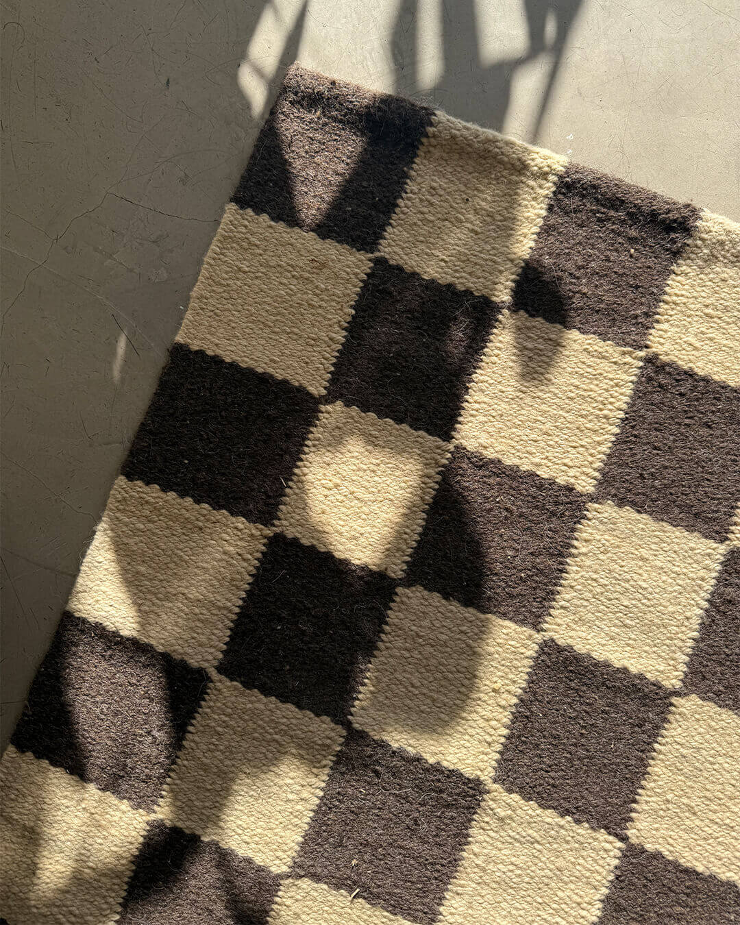 Top view of a handwoven wool rug with black and sand checkered squares laid on a smooth concrete floor.