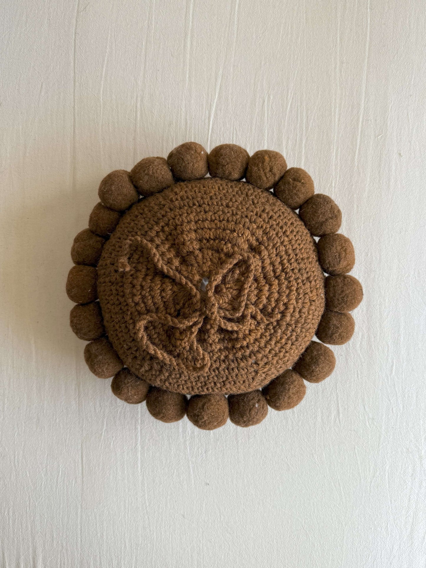 Chocolate Brown-colored round cushion with handmade pom poms, shown from the back.