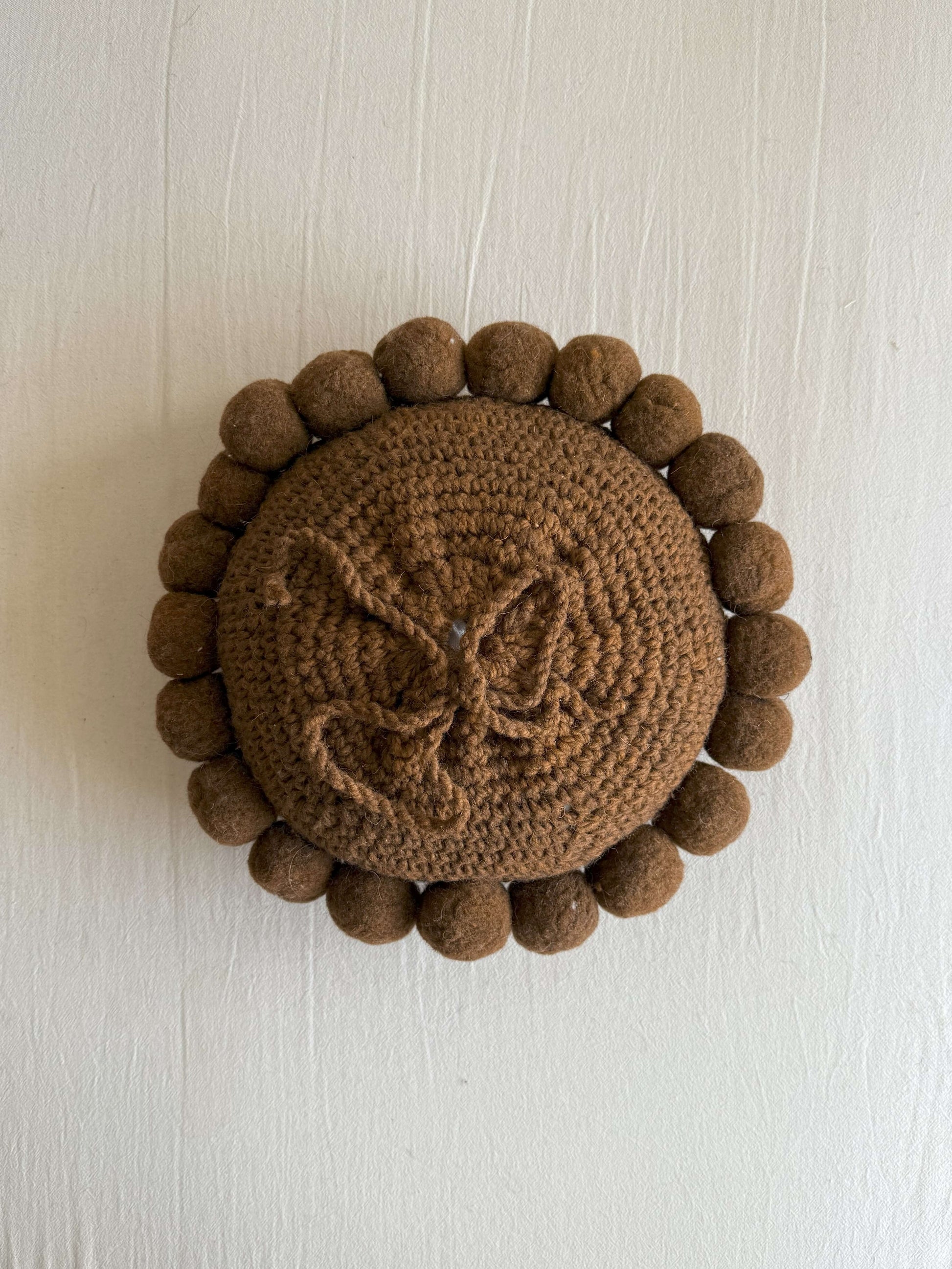 Chocolate Brown-colored round cushion with handmade pom poms, shown from the back.