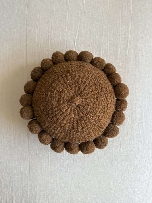 Chocolate Brown-colored round cushion with handmade pom poms, shown from the front.