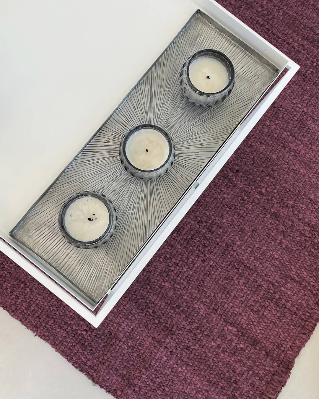 Top view of a handwoven wool rug in malbec tone with a rectangular tray and three candles resting on the textured surface.