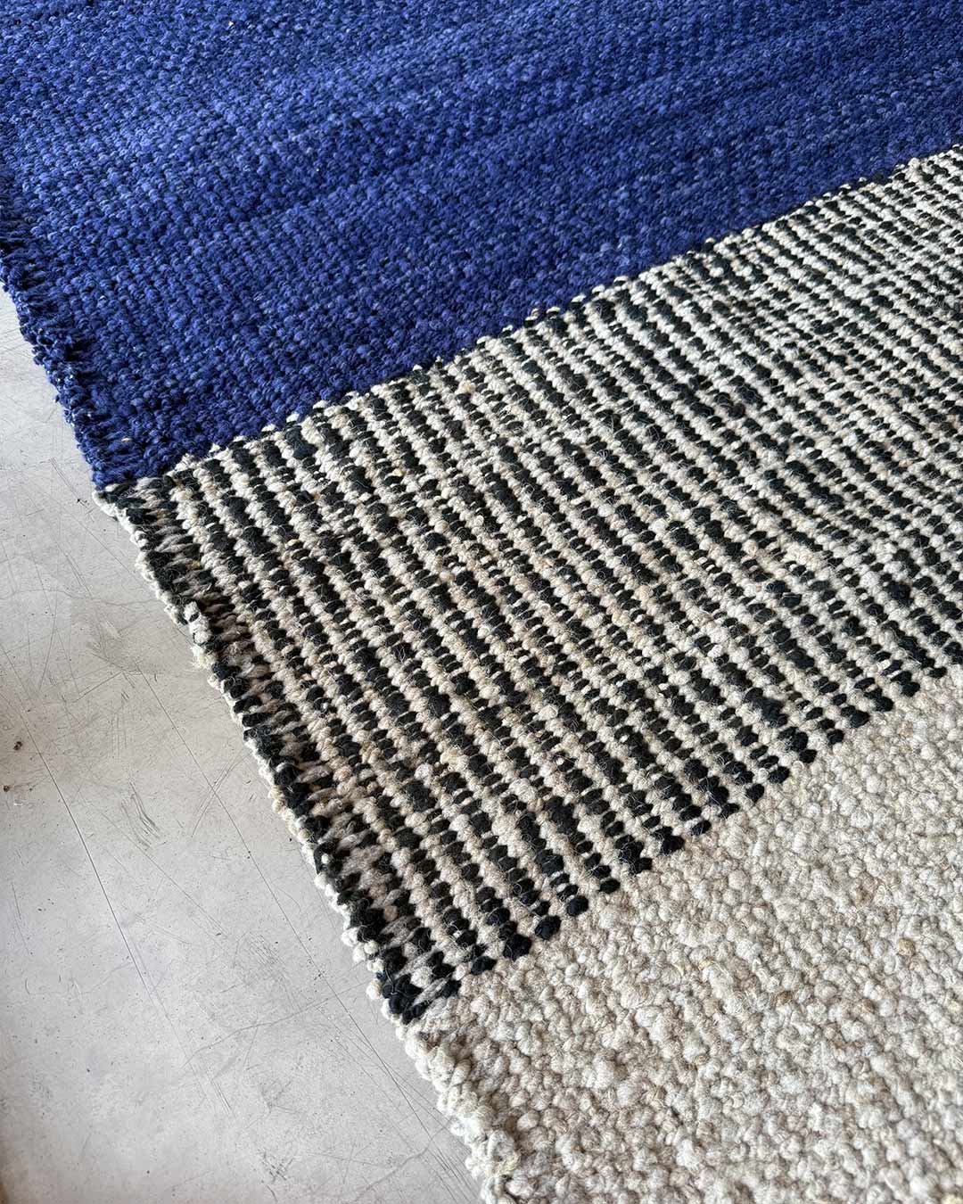 Angled corner detail of a handwoven rug where midnight blue wool meets a black-and-natural woven pattern.