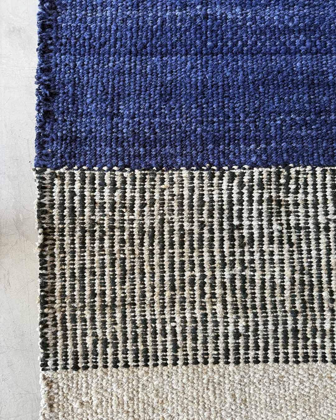Section detail of a handwoven rug showing horizontal blocks in midnight blue, black-and-natural, and undyed wool.