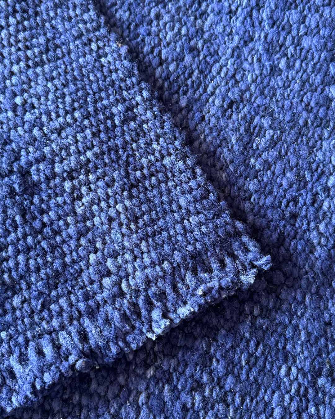Close-up of a handwoven rug highlighting the dense texture of midnight blue wool and the raw edge finish.