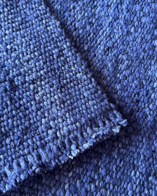 Close-up of a handwoven rug highlighting the dense texture of midnight blue wool and the raw edge finish.