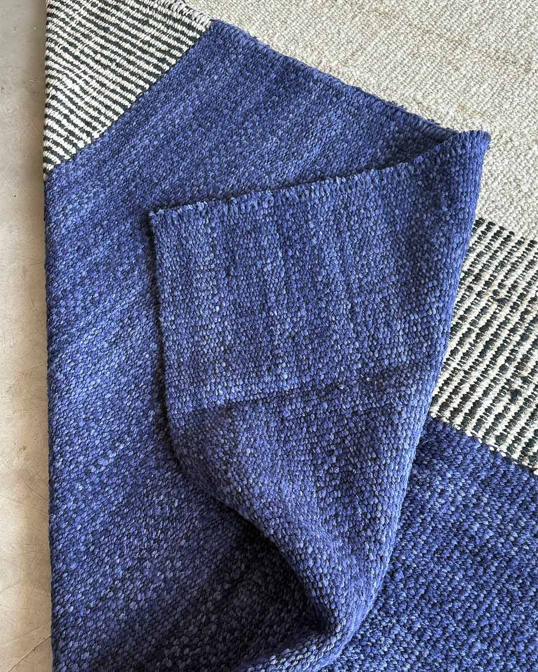 Detail view of a handwoven rug with folded midnight blue wool revealing the thickness and softness of the weave.