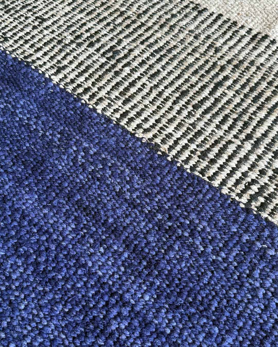 Close-up of a handwoven rug showing the junction between midnight blue wool and black-and-natural textured sections.
