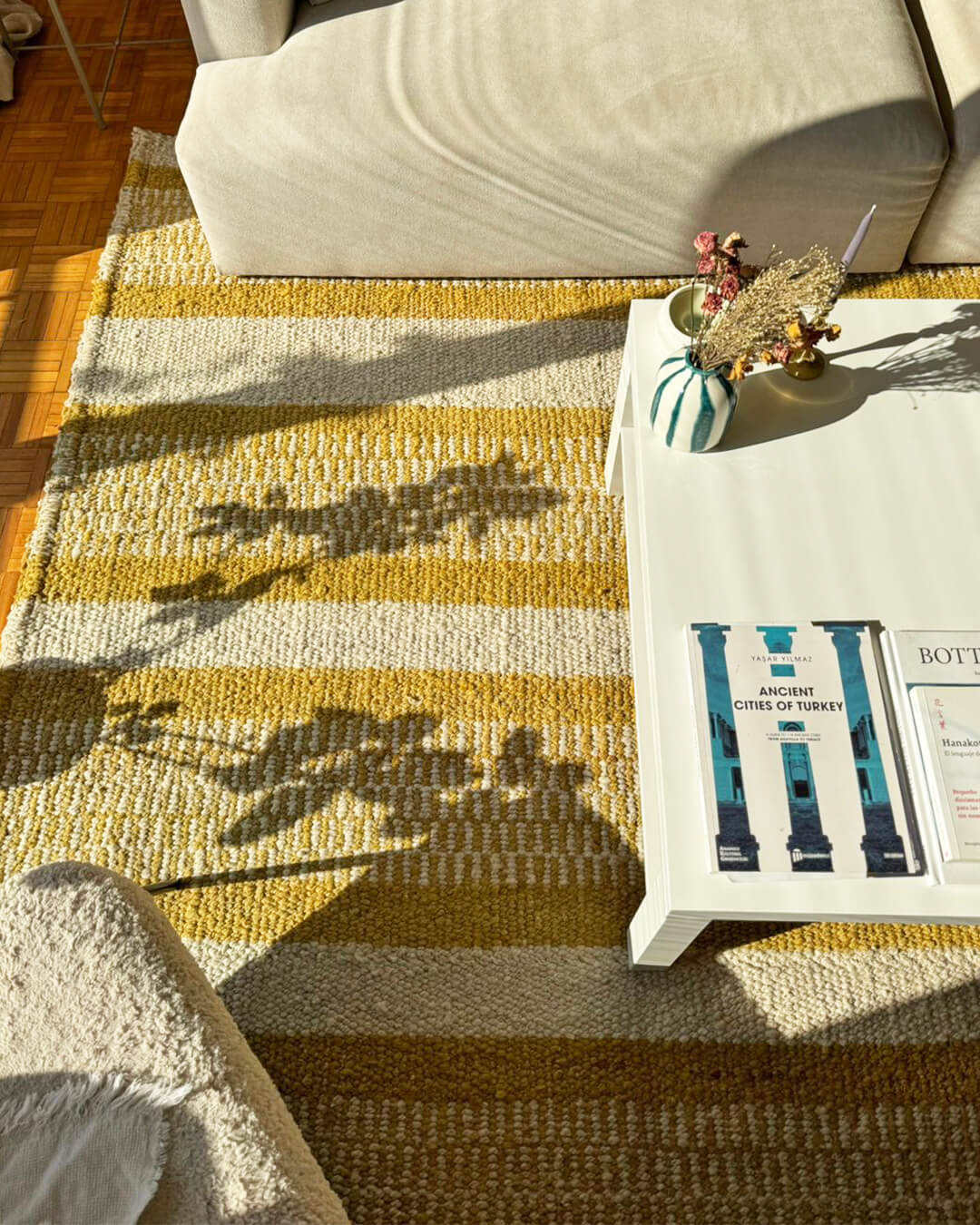 Top view of a handwoven wool rug with natural and onion stripes, shown beneath a coffee table with books and decorative objects.