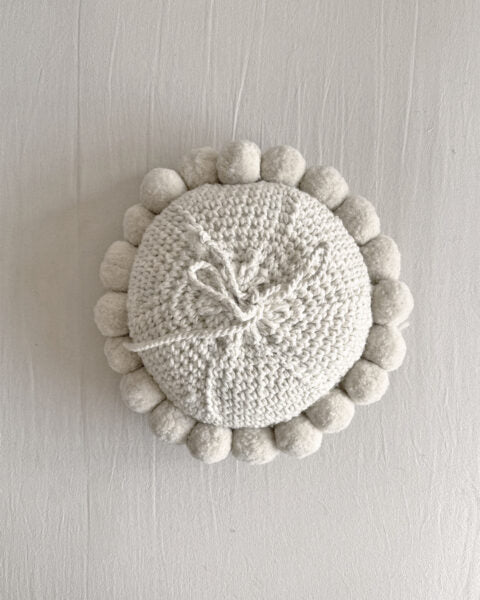 Natural White-colored round cushion with handmade pom poms, shown from the back.