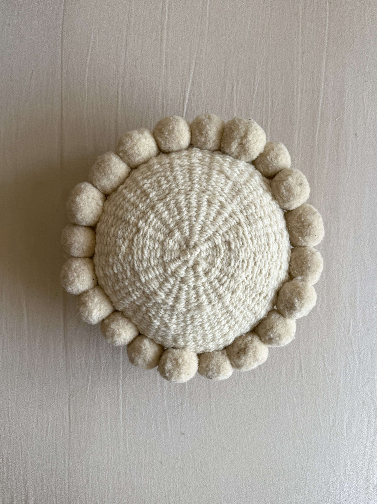 Natural White-colored round cushion with handmade pom poms, shown from the front.