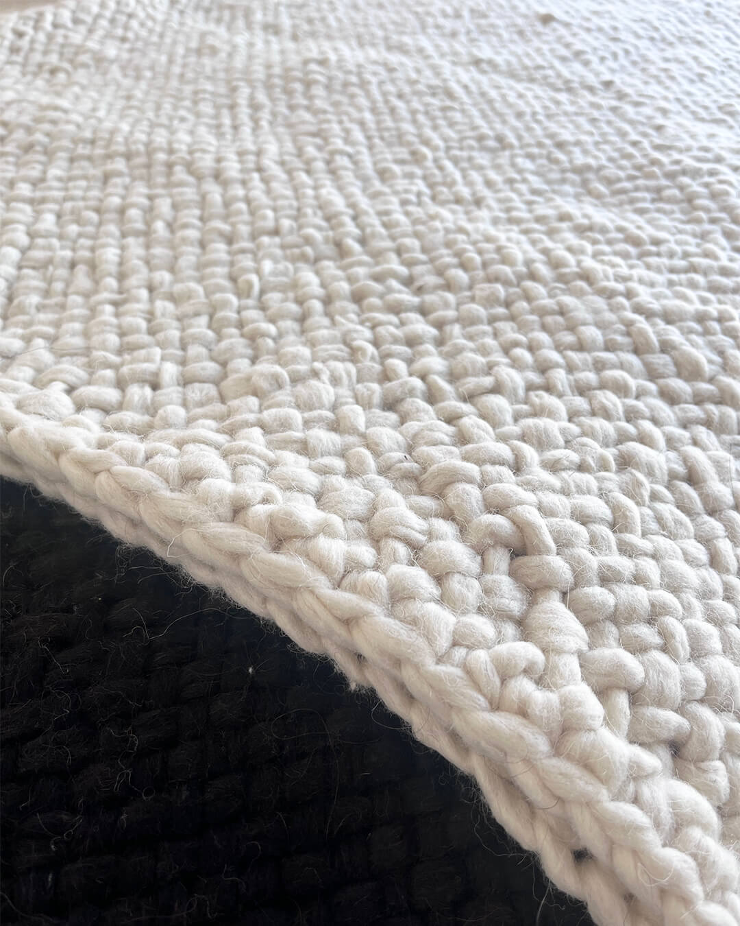 Close-up of the Natural White wool throw’s woven texture layered over another throw.