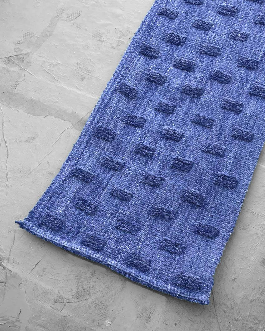 Handwoven wool rug in midnight blue with raised pom-pom texture, laid on a gray concrete floor.