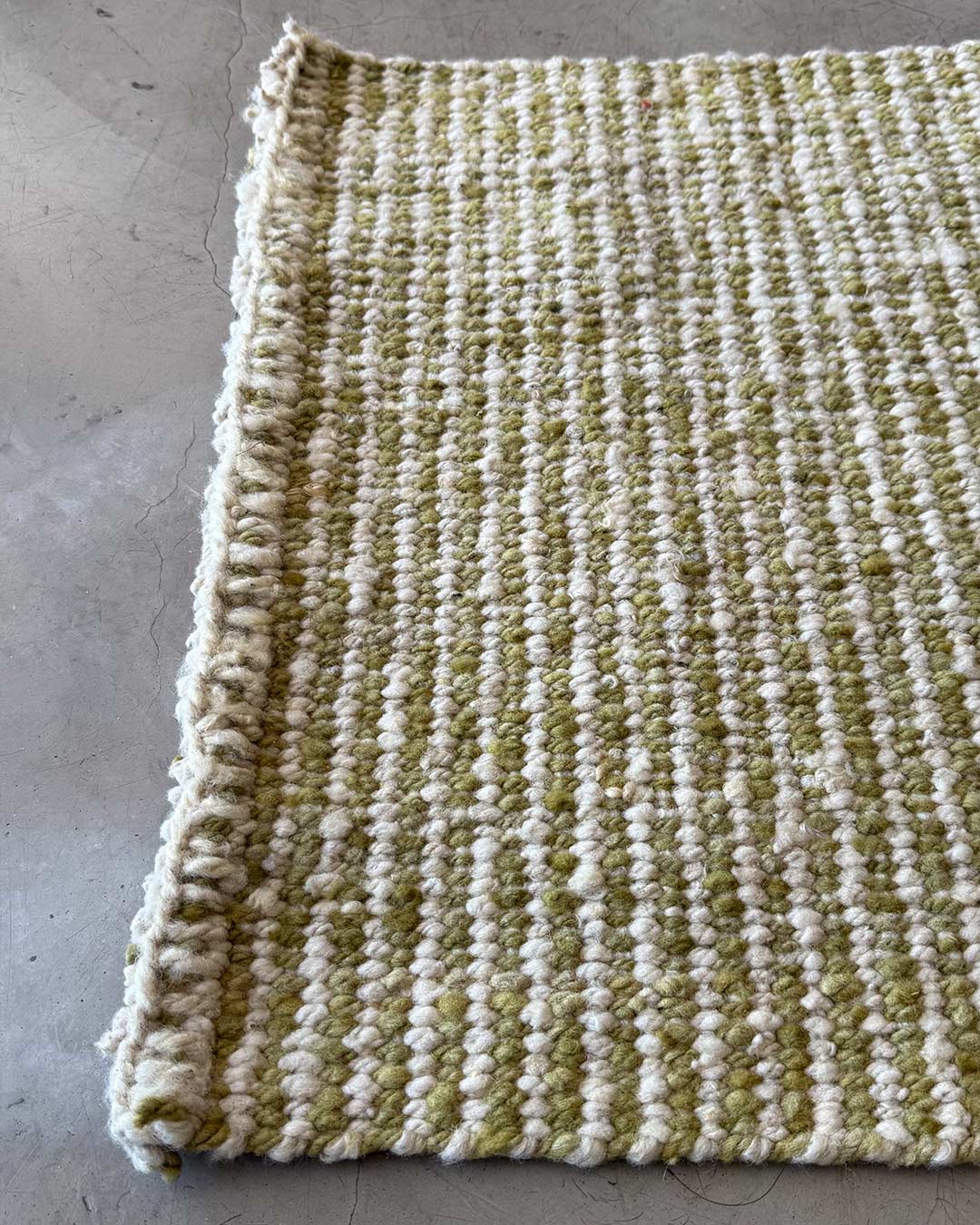 Detail of a handwoven wool runner rug in yerba green and natural with striped texture on a concrete floor.