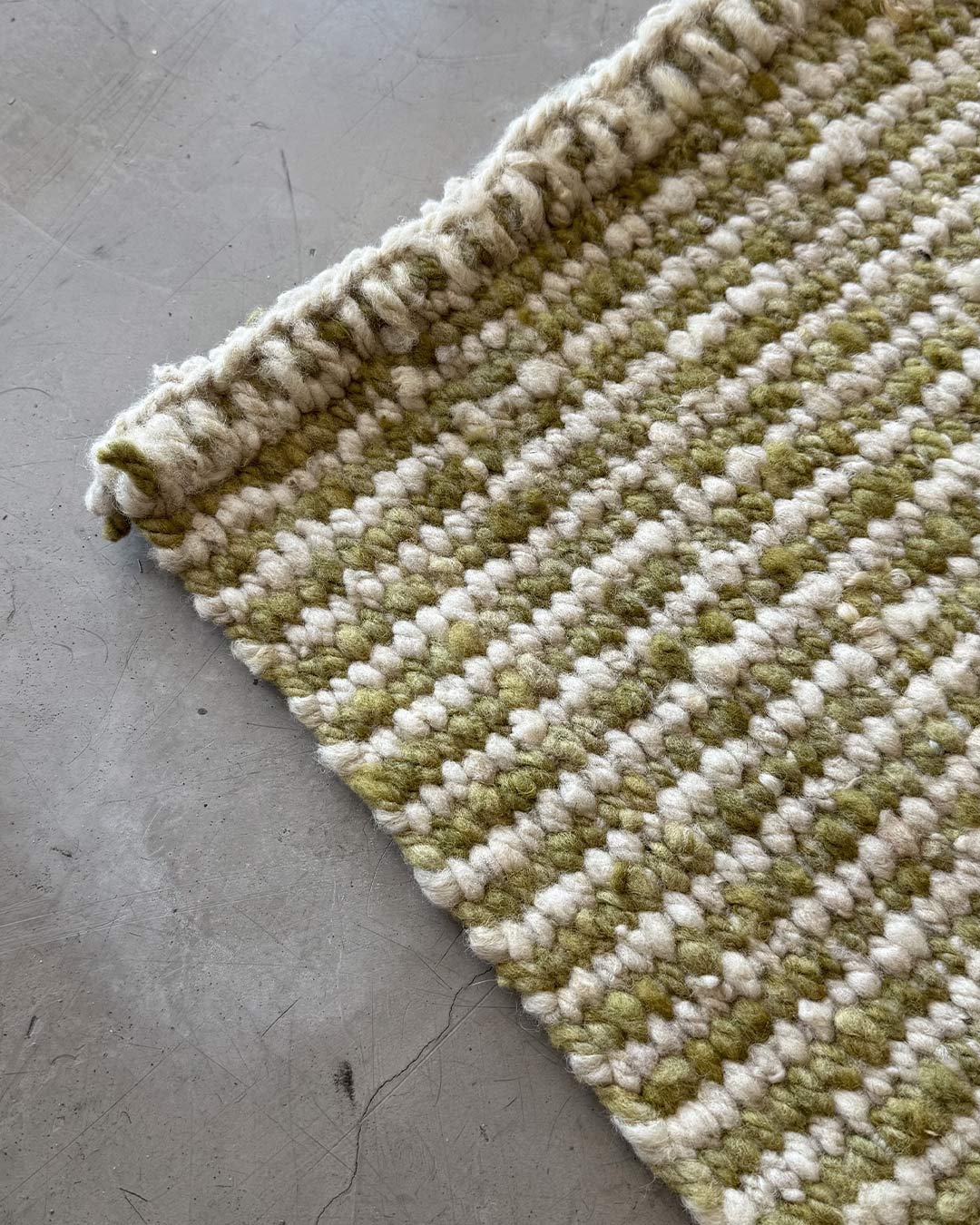 Angled detail of a handwoven yerba green and natural wool runner rug highlighting the thickness and edge finish.
