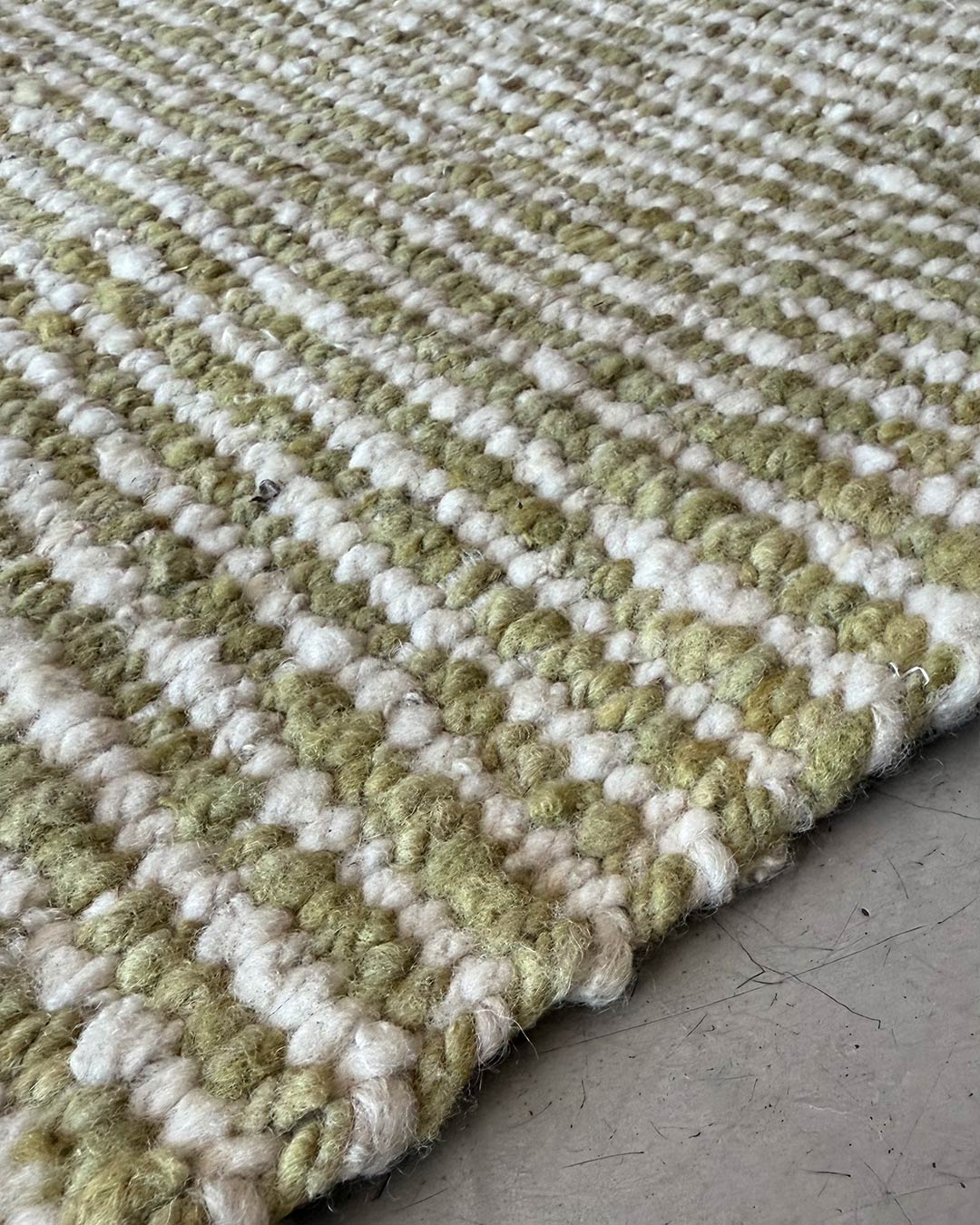 Close-up of a handwoven wool runner rug in yerba green and natural with striped texture on a concrete floor.