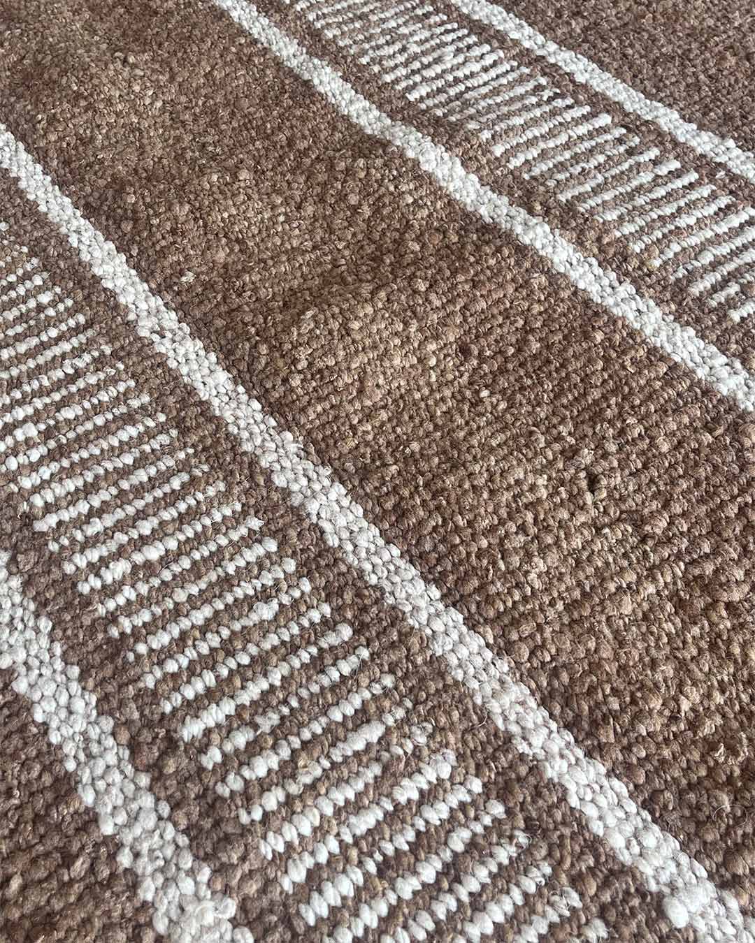 Close-up of a striped wool rug in wood and natural colors, highlighting the raised weave and alternating comb pattern.